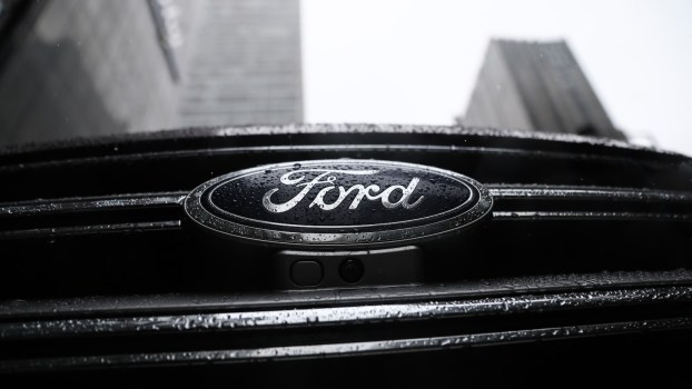 The Ford logo on the grille of a recalled crossover, tall buildings visible in the background.