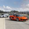 An orange Chevrolet Corvette ZR1X convertible parked in front of a silver coupe, a race track visible in the background.